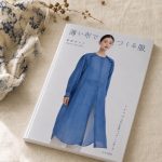 the sewing book '薄い布でつくる服' (clothes made from thin cloth) by noriko sasahara lying on natural linen, its cover showing a model in a sheer blue button-through dress.
