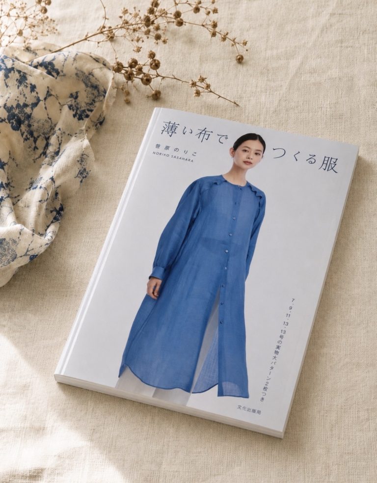 the sewing book '薄い布でつくる服' (clothes made from thin cloth) by noriko sasahara lying on natural linen, its cover showing a model in a sheer blue button-through dress.