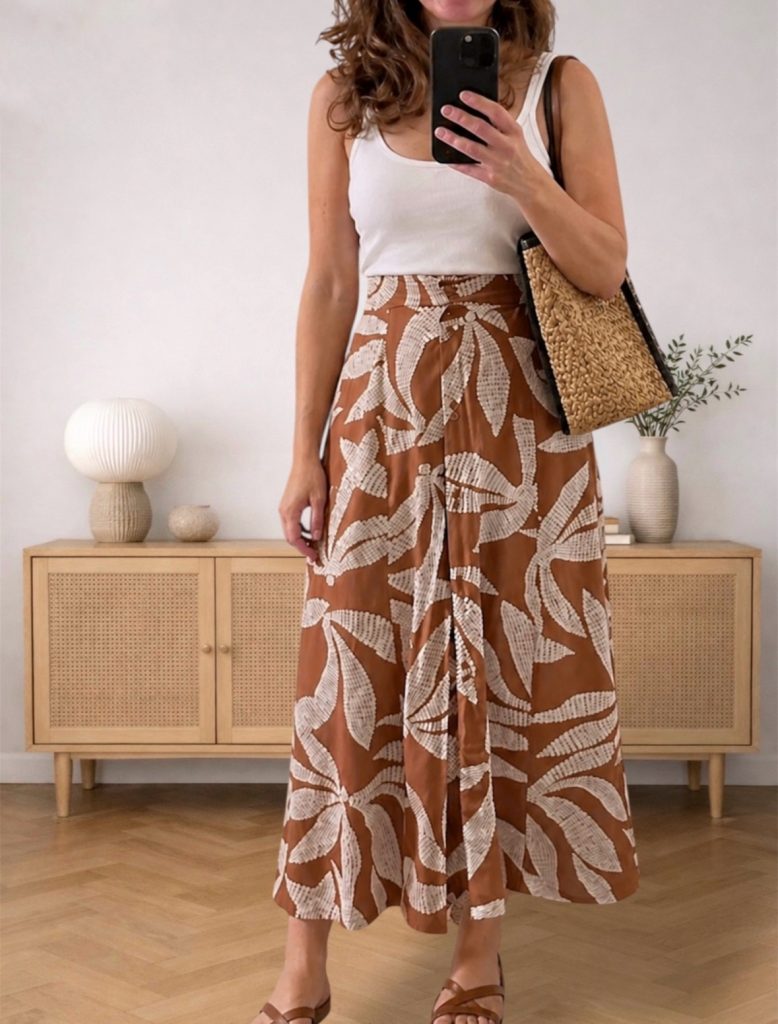 mirror selfie in a white tank top and brown leaf-print la jupe skirt with a straw bag